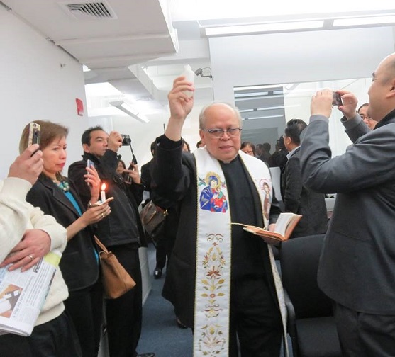 Amid lighted candles and snapping smartphones, Msgr. Oscar Aquino performs blessing of the PAL and PNB office and offers prayers. Photo by Lumen Castaneda 